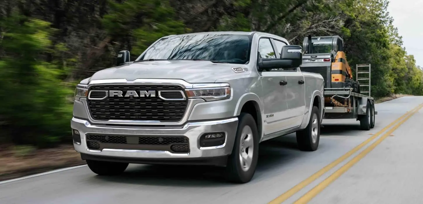 Ram 1500 Tradesman crew cab in silver towing a compact track loader on a trailer