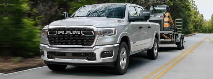 Ram 1500 Tradesman crew cab in silver towing a compact track loader on a trailer