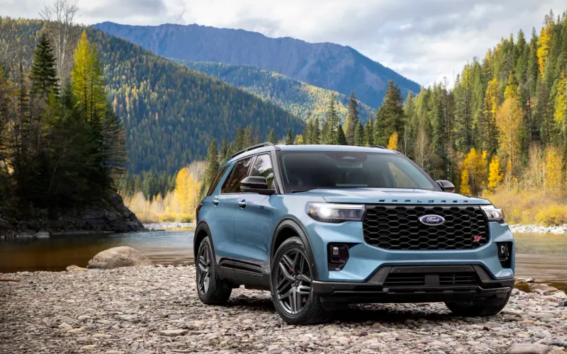 Ford Explorer ST in blue parked on a rocky riverbank below autumn mountains