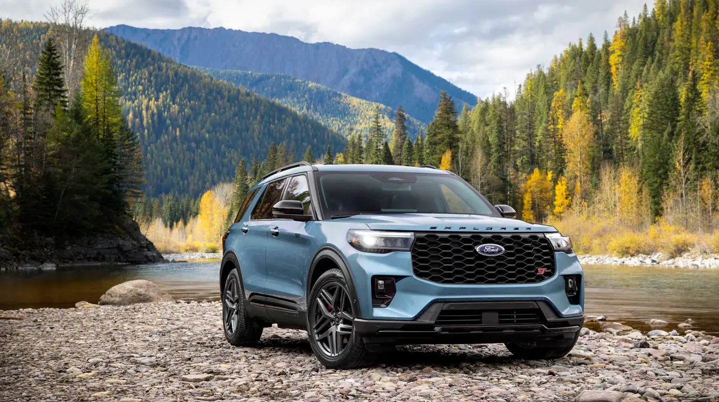 Ford Explorer ST in blue parked on a rocky riverbank below autumn mountains