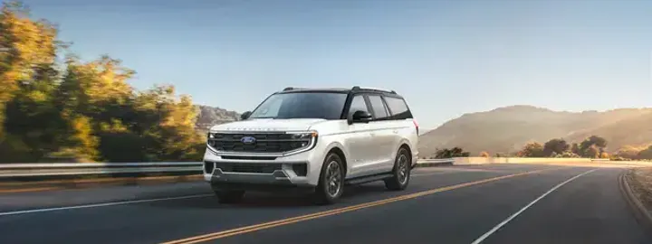 Ford Expedition in white driving a winding highway at sunset