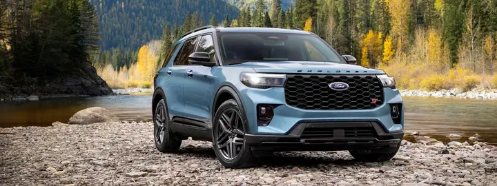 Ford Explorer ST in blue parked on a rocky riverbank below autumn mountains