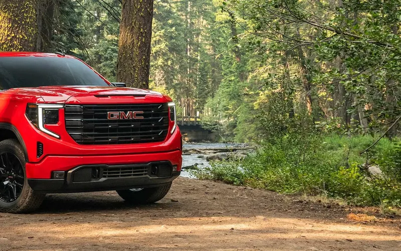 GMC Sierra 1500 crew cab in red on a dirt road through a forest