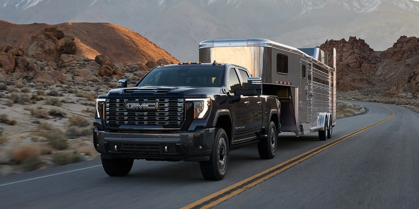 GMC Sierra HD Denali crew cab towing a gooseneck trailer on a mountain highway