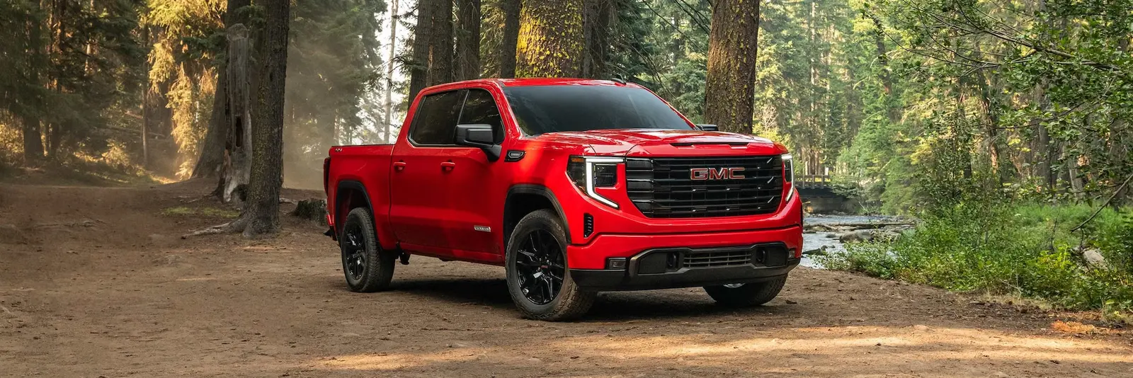 GMC Sierra 1500 crew cab in red on a dirt road through a forest