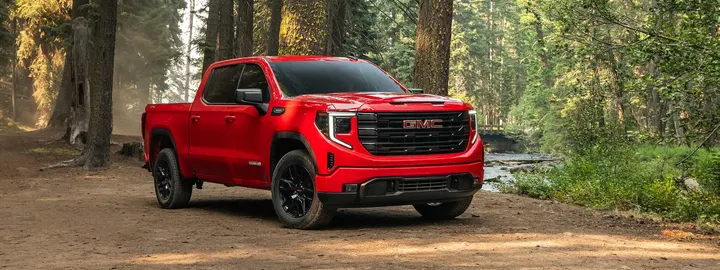 GMC Sierra 1500 crew cab in red on a dirt road through a forest