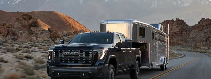 GMC Sierra HD Denali crew cab towing a gooseneck trailer on a mountain highway