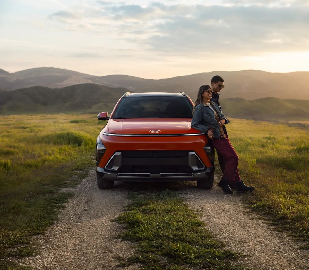 Couple leaning on the front of an orange Hyundai Kona on a dirt road
