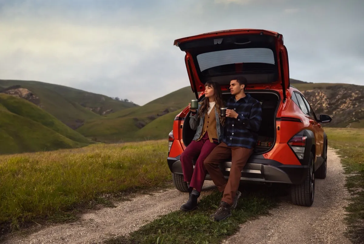 Couple sitting in the open cargo area of an orange Hyundai Kona