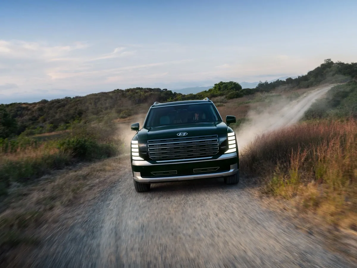 Dark green Hyundai Palisade driving down a dusty country road