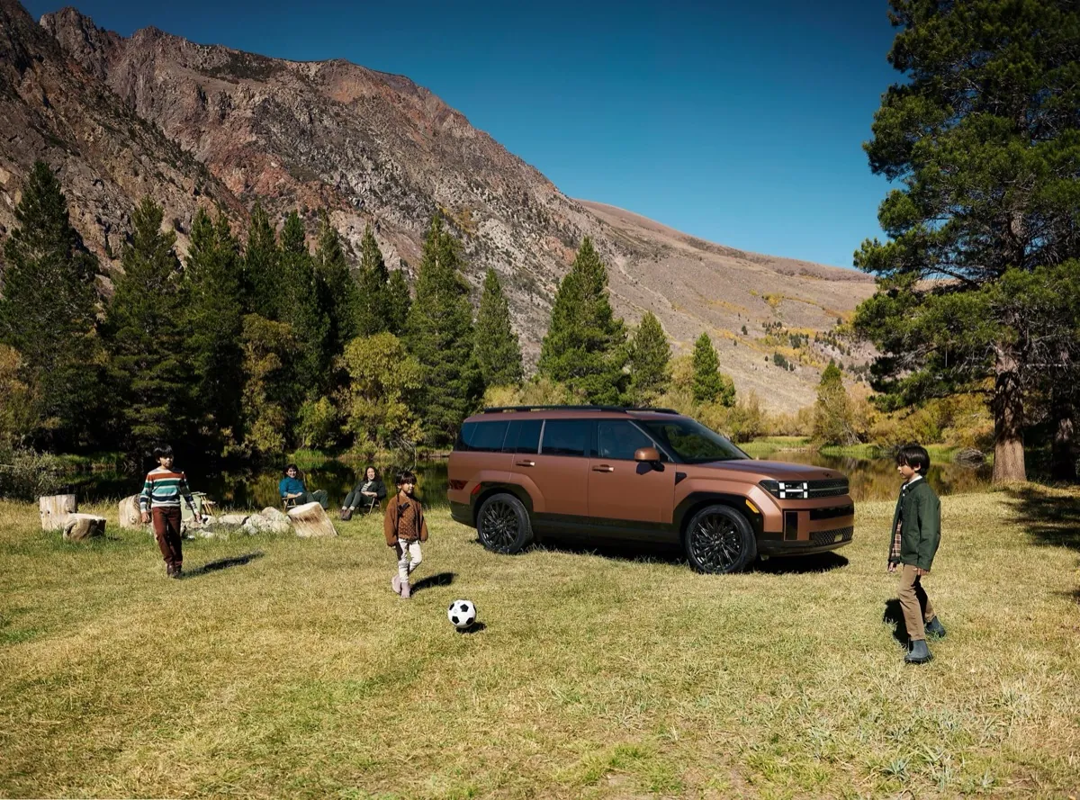 Family playing soccer beside a bronze 2027 Hyundai Santa Fe in a mountain meadow