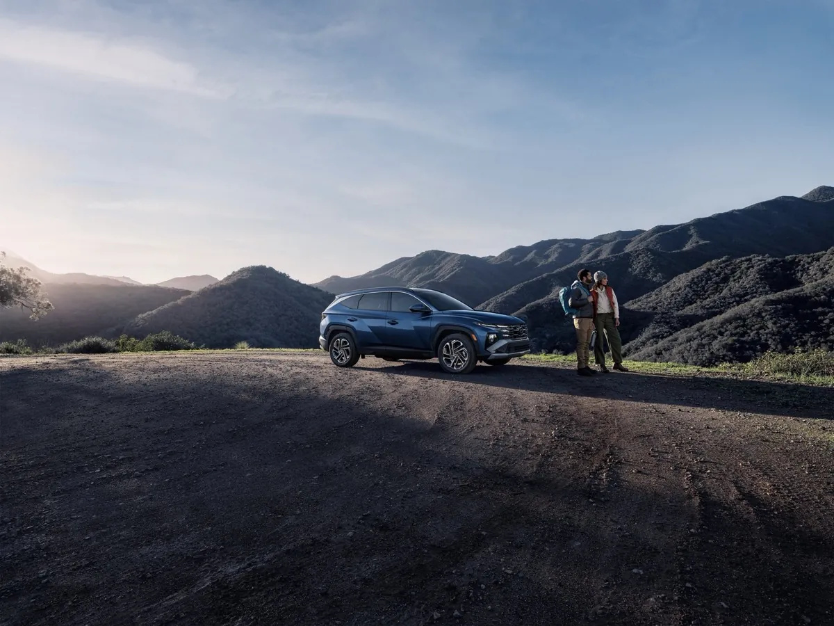 Couple standing beside a blue 2026 Hyundai Tucson on a mountain overlook