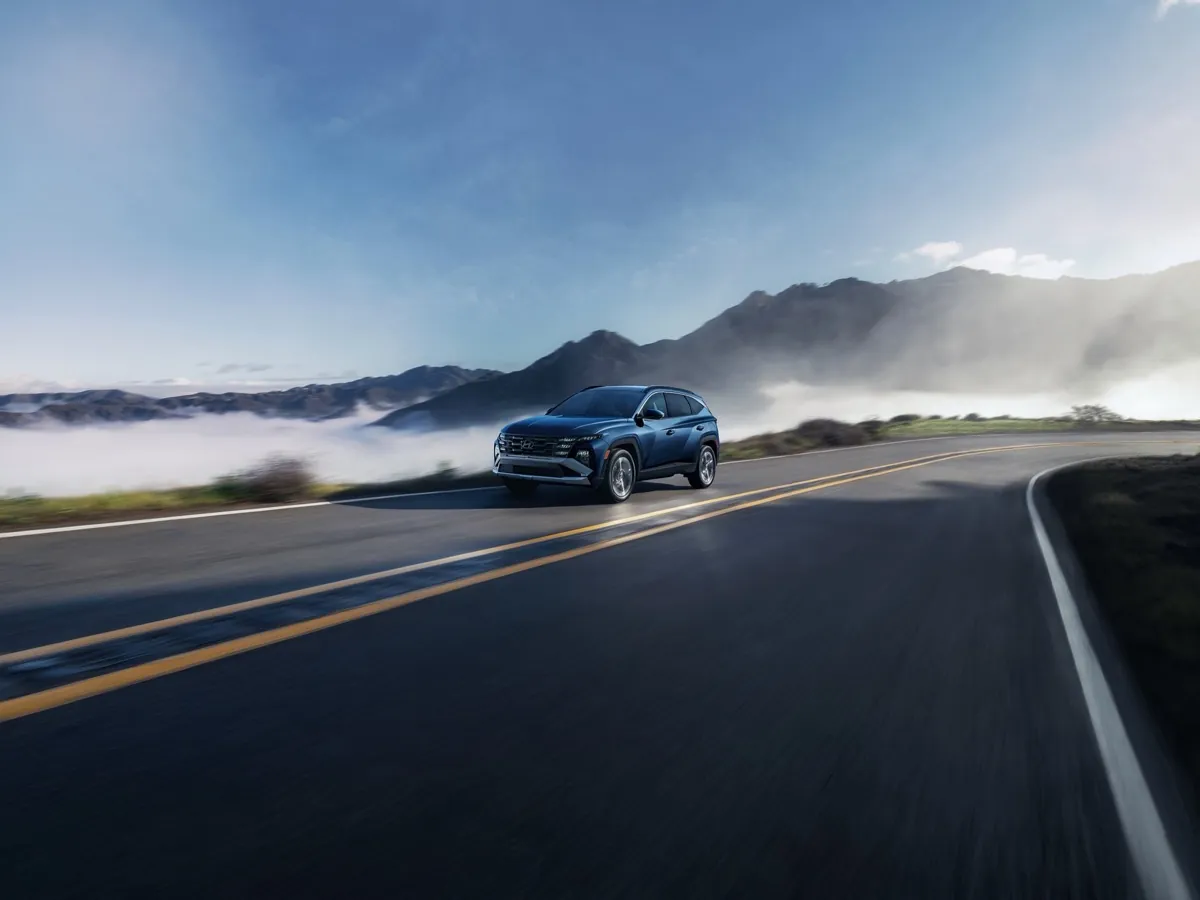 Blue 2026 Hyundai Tucson driving a mountain road above the clouds
