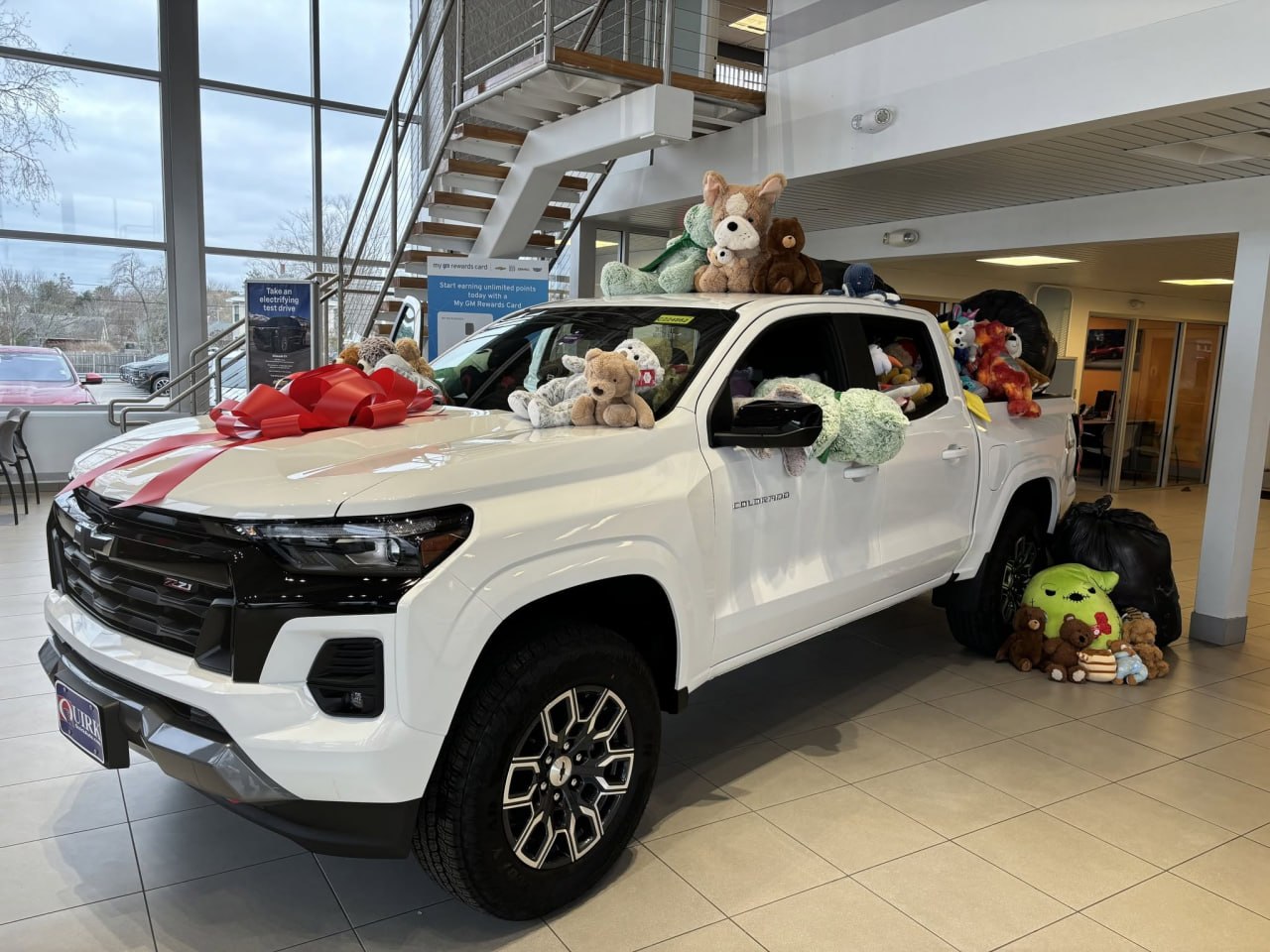 The loaded Colorado in the Quirk Chevrolet of Portland showroom, bears on the roof and hood and filled donation bags stacked beside it